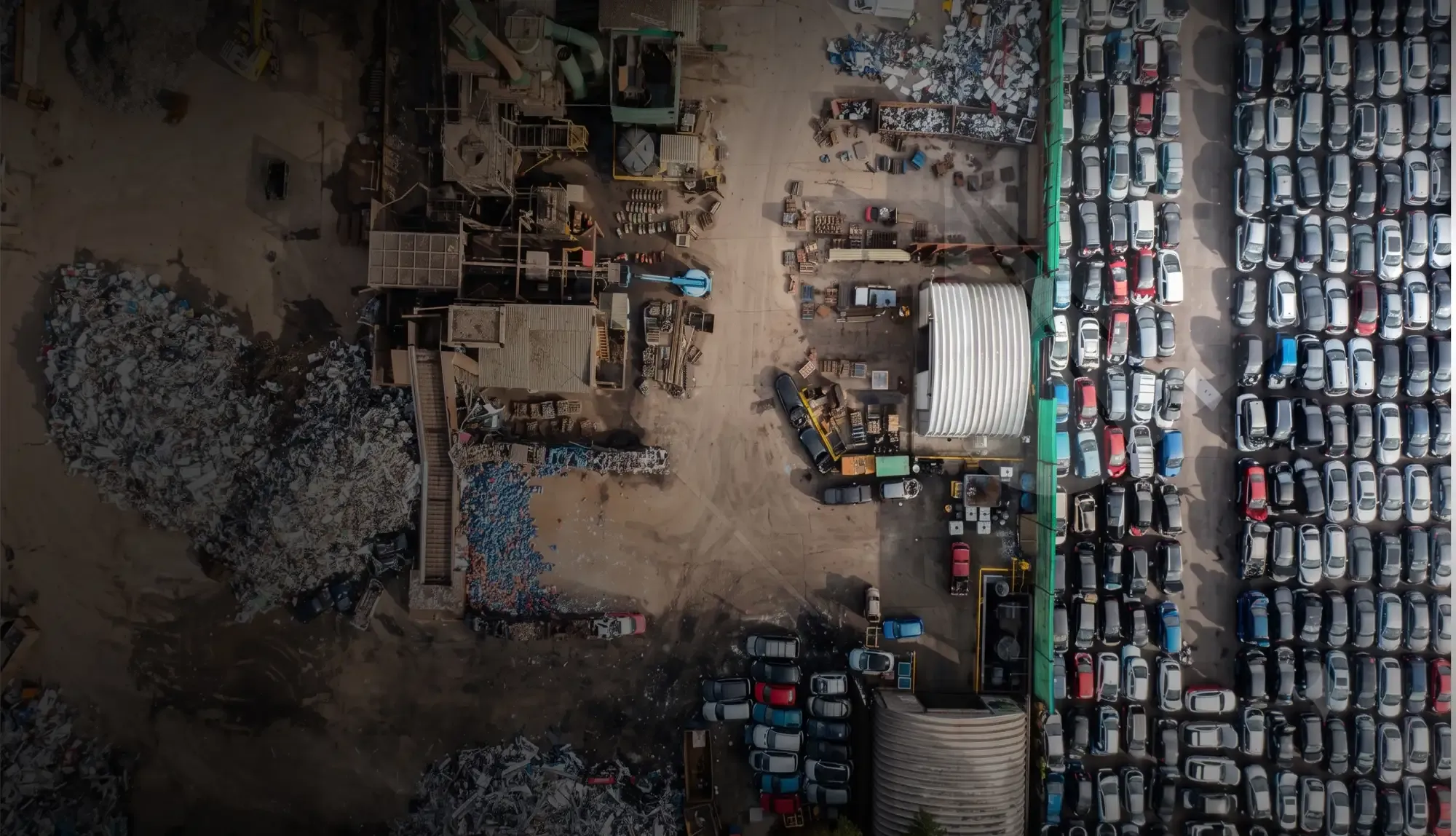 Aerial view of a vehicle salvage yard, with end-of-life cars lined up in rows beside sorted material