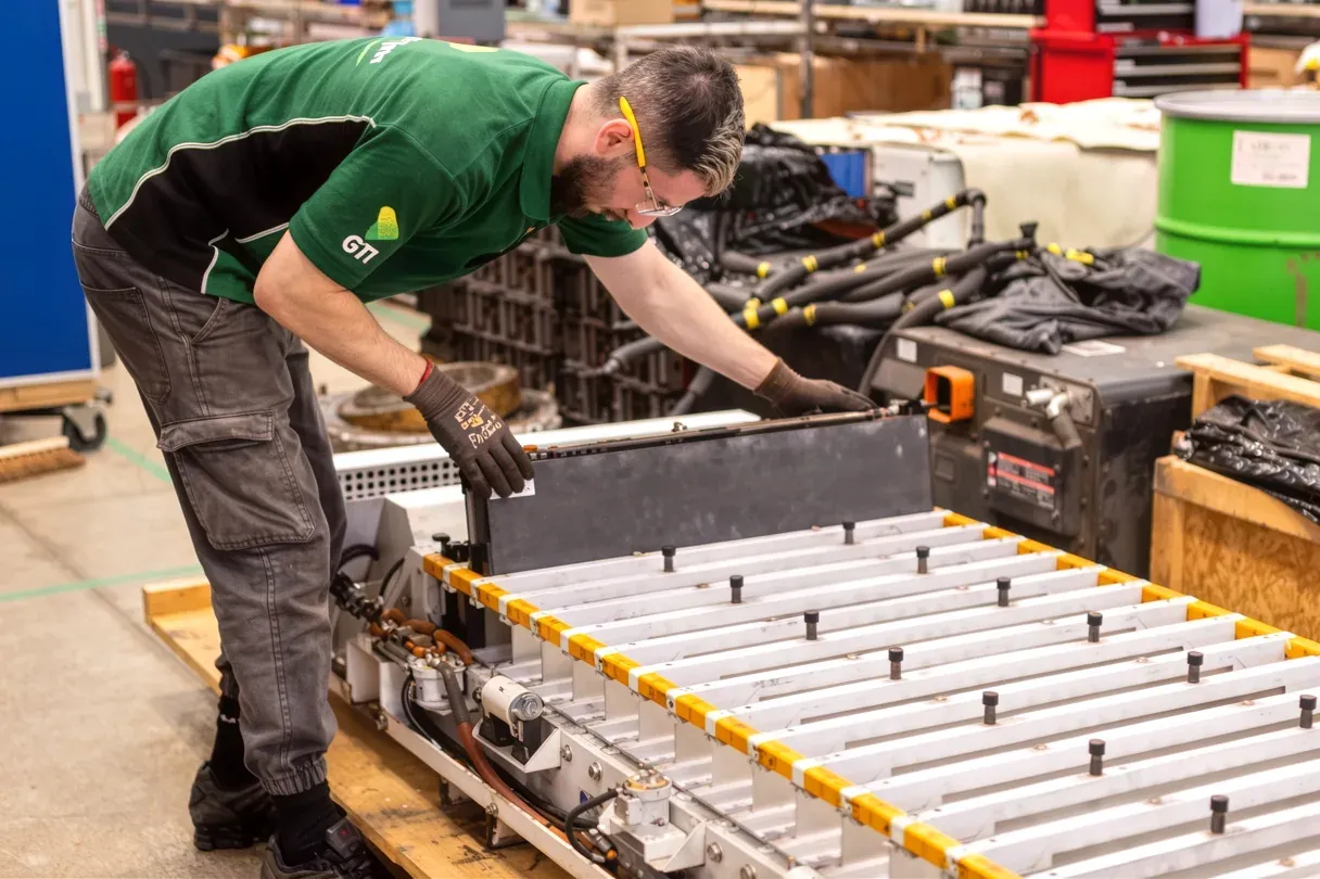 A GTI technician lifting a module out of a large white battery pack on the workshop floor