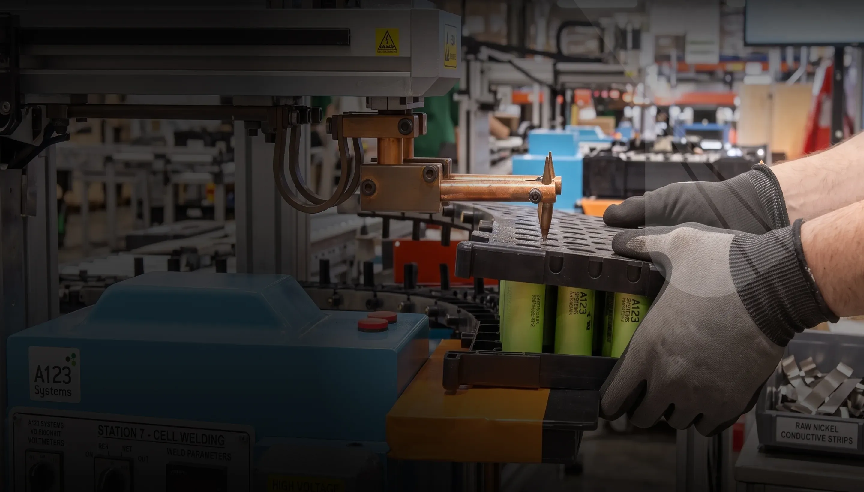 Gloved hands lifting a battery module at a workbench in the facility
