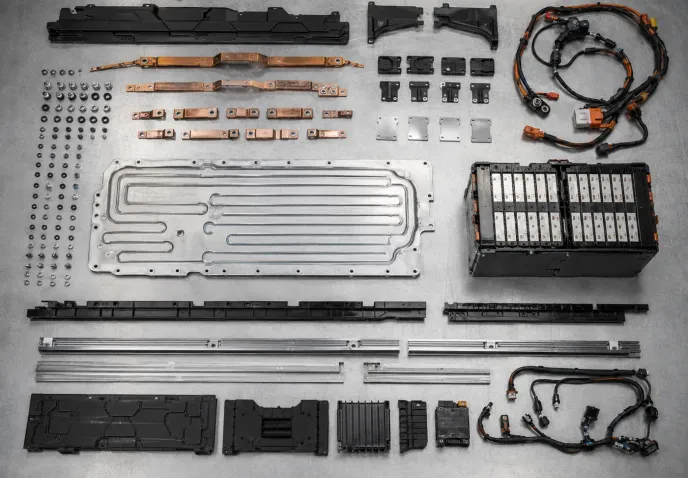 The recovered components of one battery pack laid out in ordered rows on a steel bench: busbars, cooling plate, fasteners, wiring harness and an intact module