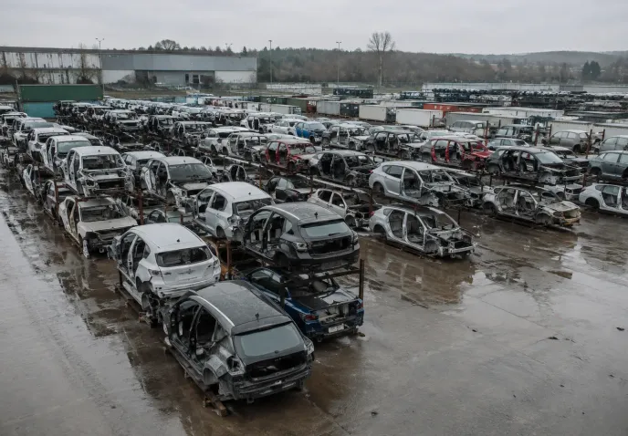 Rows of stripped end-of-life car shells racked two high across a wet storage yard, seen from above