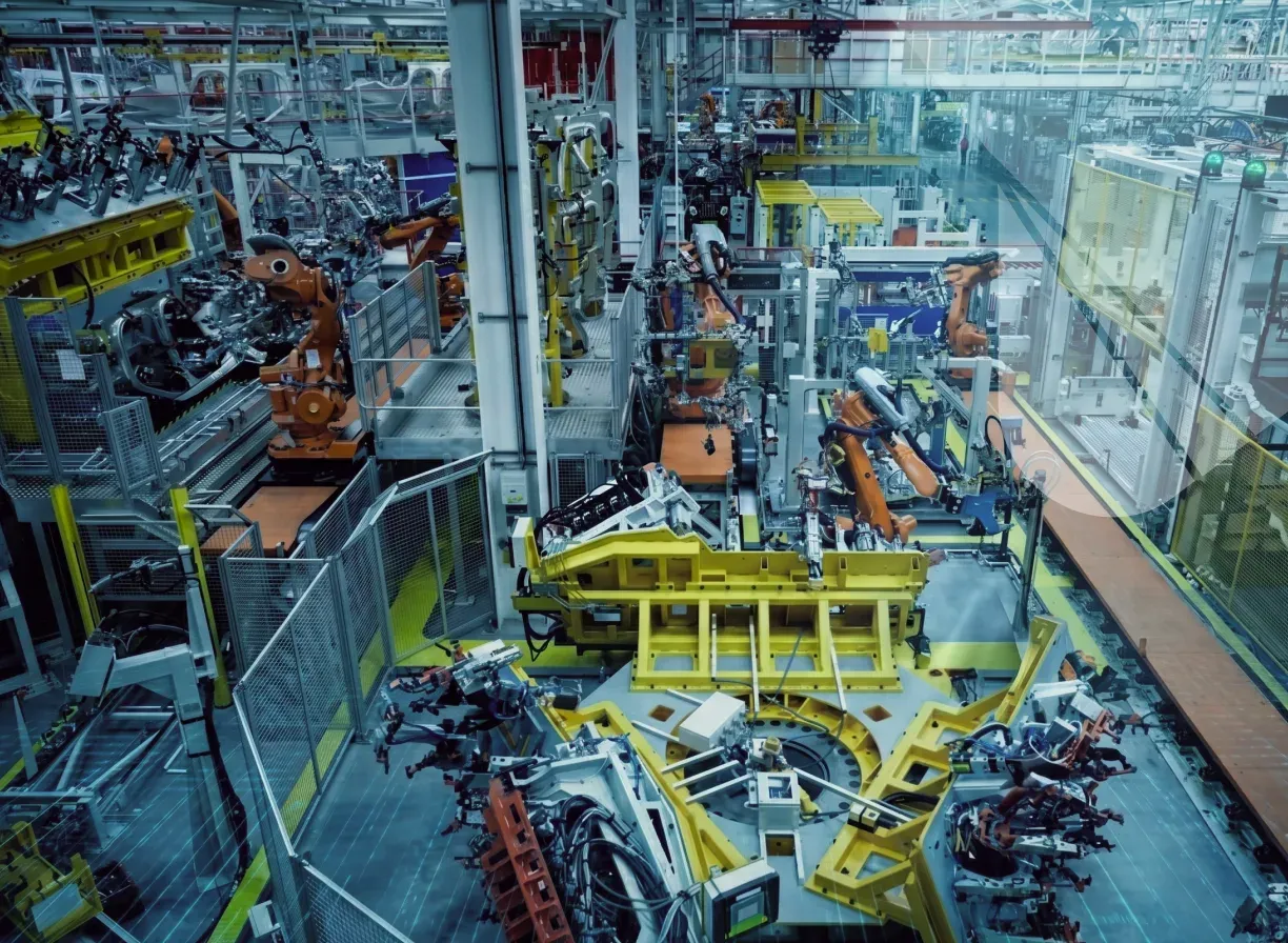 A robotic vehicle assembly line seen from above, with orange robot arms working along a yellow body jig